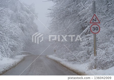 Snowy driveway and road sign speed limit 30 km. Winter forest after snowfall. Bad weather, fall. Snowy driveway and road sign speed limit 30 km. Winter forest after snowfall. Bad weather, fall. 136042009