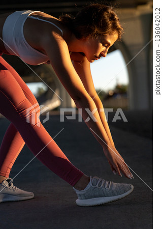 Warmup exercise before jogging: attractive female runner bend to leg warming up for running workout Warmup exercise before jogging: attractive female runner bend to leg warming up for running workout 136042012