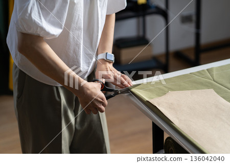 Tailor cut fabric pattern for garment. Female sewer hand hold scissors, material on table in studio Tailor cut fabric pattern for garment. Female sewer hand hold scissors, material on table in studio 136042040