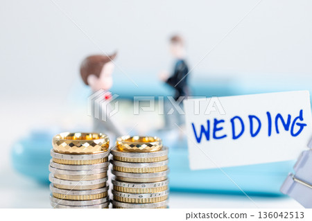 Gold wedding rings rest on stacked coins next to WEDDING card clipped on blue calculator, blurred groom figurines behind for all couples, symbolizing inclusive budgeting, equality. inclusive budgeting Gold wedding rings rest on stacked coins next to WEDDING card clipped on blue calculator, blurred groom figurines behind for all couples, symbolizing inclusive budgeting, equality. inclusive budgeting 136042513