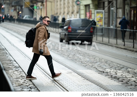 Stylish man crossing a cobblestone street in a vibrant urban setting during a chilly afternoon, showcasing a blend of fashion and city life Stylish man crossing a cobblestone street in a vibrant urban setting during a chilly afternoon, showcasing a blend of fashion and city life 136042516