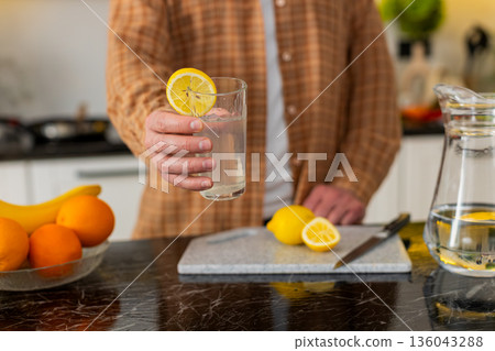 Unrecognizable man making lemon water in kitchen for healthy hydration morning wellness routine Unrecognizable man making lemon water in kitchen for healthy hydration morning wellness routine 136043288