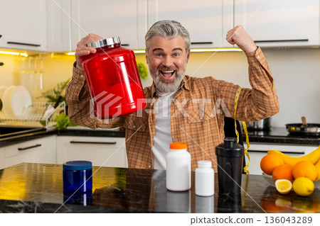 Middle-aged man shows new protein supplement jar in kitchen celebrating fitness weight loss success Middle-aged man shows new protein supplement jar in kitchen celebrating fitness weight loss success 136043289