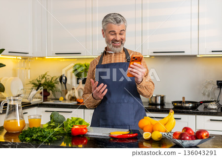Mature man celebrating big smartphone victory win in home kitchen after online success notification 136043291