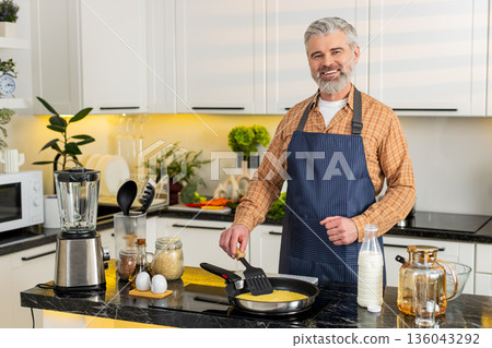 Middle-aged man pouring raw omelet mix into frying pan in home kitchen for healthy diet breakfast. Middle-aged man pouring raw omelet mix into frying pan in home kitchen for healthy diet breakfast. 136043292