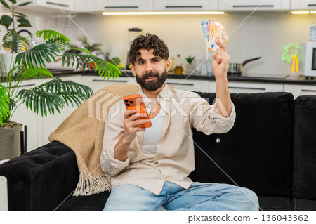 Indian man counting euro money cash salary using smartphone calculator for vacation budget future 136043362