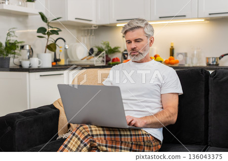 Middle-aged man with laptop on knees writes resume or works freelance remote work focused profile Middle-aged man with laptop on knees writes resume or works freelance remote work focused profile 136043375