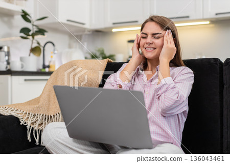 Young woman holds temples from laptop headache squints tries to rest and ease pain after long work 136043461