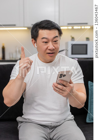 Asian man studies online course on smartphone in headphones finds solution shows ok sign sets goal 136043467