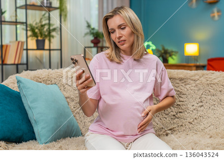 Pregnant woman sighing disappointed scrolling smartphone after losing online game showing sad mimic Pregnant woman sighing disappointed scrolling smartphone after losing online game showing sad mimic 136043524
