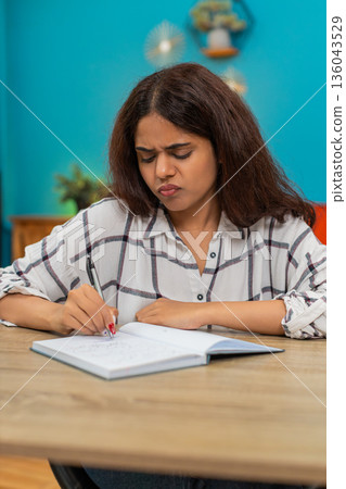 Indian woman writes in notebook crosses out lines then retries searching solution focused determined 136043529