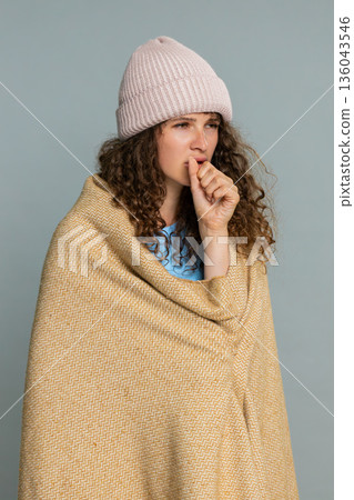 Woman coughing cold symptoms wrapped blanket wearing hat feeling unwell sick flu illness reaction Woman coughing cold symptoms wrapped blanket wearing hat feeling unwell sick flu illness reaction 136043546
