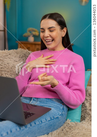 Young woman on sofa watching funny video on laptop screen laughing joyfully at amusing content Young woman on sofa watching funny video on laptop screen laughing joyfully at amusing content 136044053