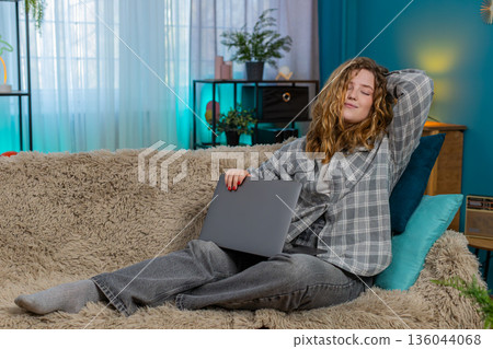 Young woman on sofa yawning stretching closing laptop after long work feeling happy and satisfied 136044068