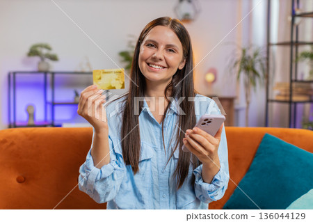 Happy young woman doing payments online purchase shopping in internet store holding bank credit card 136044129