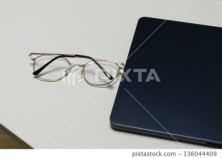Glasses are placed on a laptop in a simple workspace. The setup shows a focused environment for work or study 136044409