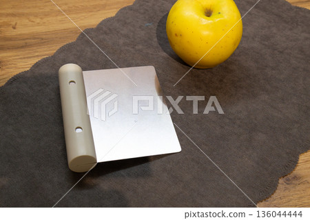 A yellow apple sits next to a gray kitchen tool on brown cloth in a home kitchen during evening hours A yellow apple sits next to a gray kitchen tool on brown cloth in a home kitchen during evening hours 136044444