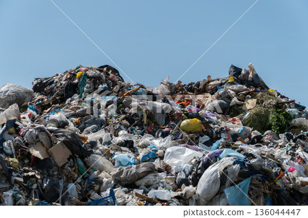 A large heap of trash sits under a clear sky, showcasing various discarded materials and the impact of waste on the environment 136044447