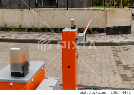 An automatic barrier gate waits for incoming vehicles in a newly paved parking area, surrounded by modern architecture and greenery An automatic barrier gate waits for incoming vehicles in a newly paved parking area, surrounded by modern architecture and greenery 136044451