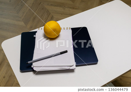A vibrant lemon adds a cheerful touch atop a clean notebook and sleek laptop, inviting creativity during a quiet work session A vibrant lemon adds a cheerful touch atop a clean notebook and sleek laptop, inviting creativity during a quiet work session 136044479