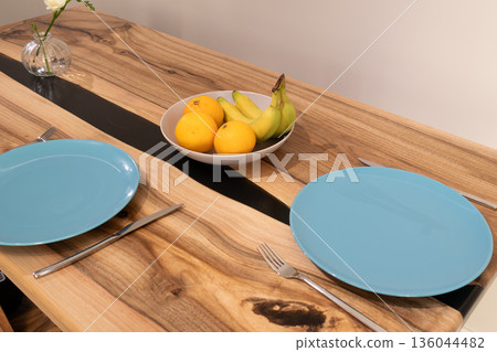 A tranquil kitchen table is set with vibrant blue plates and a bowl of fresh yellow bananas and oranges, inviting shared moments and laughter A tranquil kitchen table is set with vibrant blue plates and a bowl of fresh yellow bananas and oranges, inviting shared moments and laughter 136044482