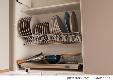 Brightly lit kitchen cabinet showcases an array of colorful plates and bowls, creatively arranged for easy access and visual delight 136044483