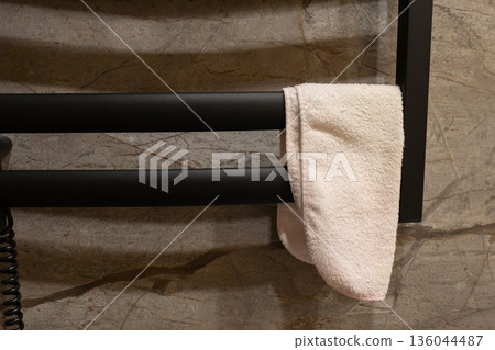 A plush white towel rests gently on a sleek black rack, highlighting the contemporary design of a luxury bathroom with elegant stone walls A plush white towel rests gently on a sleek black rack, highlighting the contemporary design of a luxury bathroom with elegant stone walls 136044487