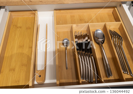 Spoons, forks, and knives rest gracefully in a bamboo drawer, creating a tidy and inviting kitchen atmosphere with natural appeal 136044492
