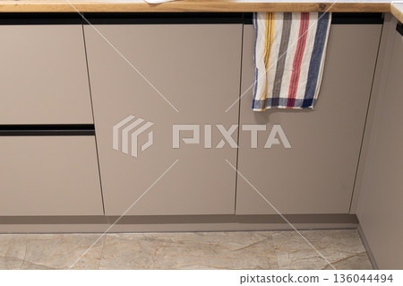 Sleek cabinets blend with a light wood countertop, while a colorful dish towel adds a touch of warmth to this contemporary kitchen space 136044494