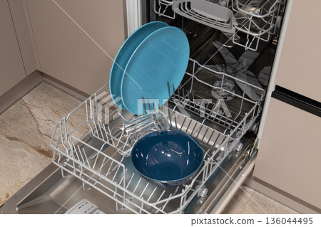 Clean blue plates and a bowl rest inside a modern dishwasher, ready for drying after a lovely family meal, showcasing kitchen efficiency and style Clean blue plates and a bowl rest inside a modern dishwasher, ready for drying after a lovely family meal, showcasing kitchen efficiency and style 136044495
