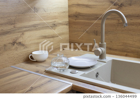 A cozy kitchen corner features warm wooden surfaces, a sleek sink, and soft lighting, creating a welcoming atmosphere for culinary creations 136044499