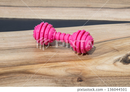 Colorful rubber dumbbell toy lies on a smooth wooden table, waiting for furry friends to engage in joyful play and exercise Colorful rubber dumbbell toy lies on a smooth wooden table, waiting for furry friends to engage in joyful play and exercise 136044501