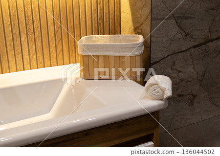 Soft light enhances the charming details of a bathroom with a bamboo basket and a neatly rolled towel on a sleek white countertop Soft light enhances the charming details of a bathroom with a bamboo basket and a neatly rolled towel on a sleek white countertop 136044502