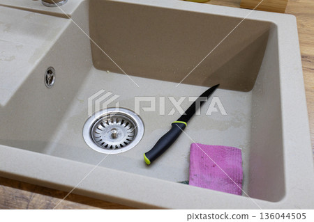 A sharp knife lies on the edge of a clean sink next to a cloth, indicating recent meal preparation in a cozy kitchen 136044505