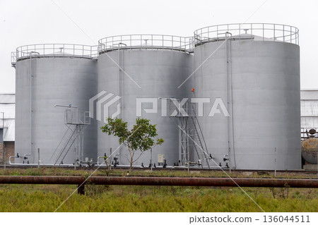 Three large silver tanks rise above the ground, surrounded by greenery, representing industrial progress in a serene rural area Three large silver tanks rise above the ground, surrounded by greenery, representing industrial progress in a serene rural area 136044511