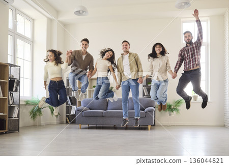 Cheerful friends jumping in home living room, celebrating success and teamwork 136044821