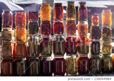 Colorful stack of pickled items in glass jars for sale at a sunny market display 136044964