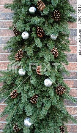 Evergreen garland with pinecone accents and silver balls on brick wall for festive decor 136045016