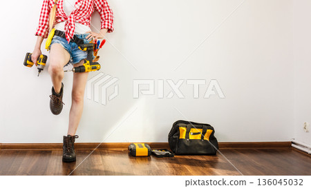 Woman wearing helmet, toolbelt about to drill wall 136045032
