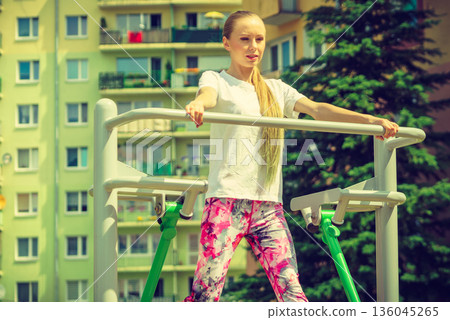 Woman doing exercise in outdoor gym Woman doing exercise in outdoor gym 136045265
