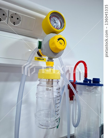 The hospital has a medical vacuum regulator and a suction canister attached to the wall. Clear tubing connects the canister to the regulator. Equipment is ready for medical procedures. 136045335