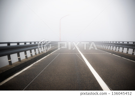 Bridge in dense fog: Road with poor visibility and guardrails obscured by white mist Bridge in dense fog: Road with poor visibility and guardrails obscured by white mist 136045452