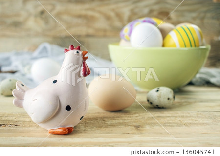 Easter chicken figurine with decorated and natural eggs on wooden background. Rustic still life with fresh farm eggs and decorative chicken figurine. Easter chicken figurine with decorated and natural eggs on wooden background. Rustic still life with fresh farm eggs and decorative chicken figurine. 136045741