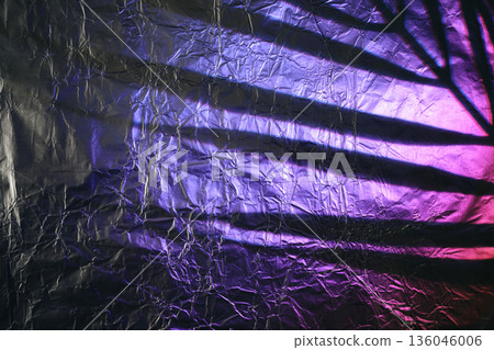 Crumpled aluminum foil surface displaying cast shadow with purple and pink light 136046006