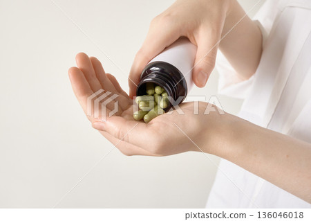 Hands pouring green herbal capsules from bottle into an open palm Hands pouring green herbal capsules from bottle into an open palm 136046018