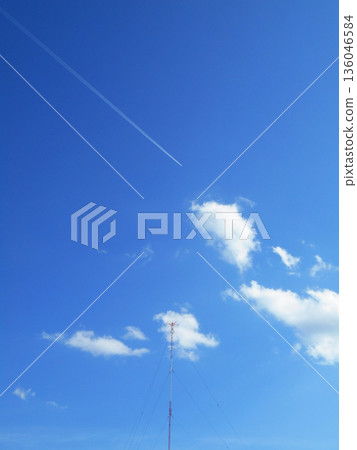A single contrail and white clouds piercing the blue sky A single contrail and white clouds piercing the blue sky 136046584