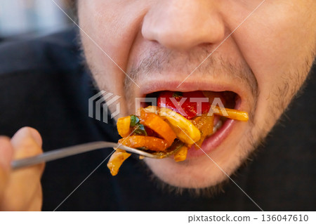 male eating a large forkful of stir fry pasta vegetables with open mouth, showcasing overeating and unhealthy eating habits. concept of obesity, diabetes, gluttony, diabetes, overeating male eating a large forkful of stir fry pasta vegetables with open mouth, showcasing overeating and unhealthy eating habits. concept of obesity, diabetes, gluttony, diabetes, overeating 136047610