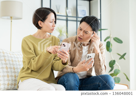一對中年夫婦在客廳使用智慧型手機 一對中年夫婦在客廳使用智慧型手機 136048001