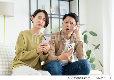 A middle-aged couple using smartphones in the living room 136048004