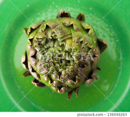 cooked whole artichoke on a green plate cooked whole artichoke on a green plate 136048263